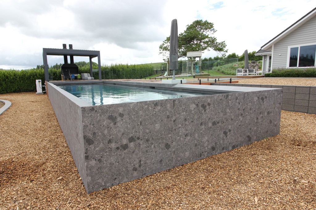 A concrete swimming pool featuring a central water fountain, surrounded by a clean, modern design.
